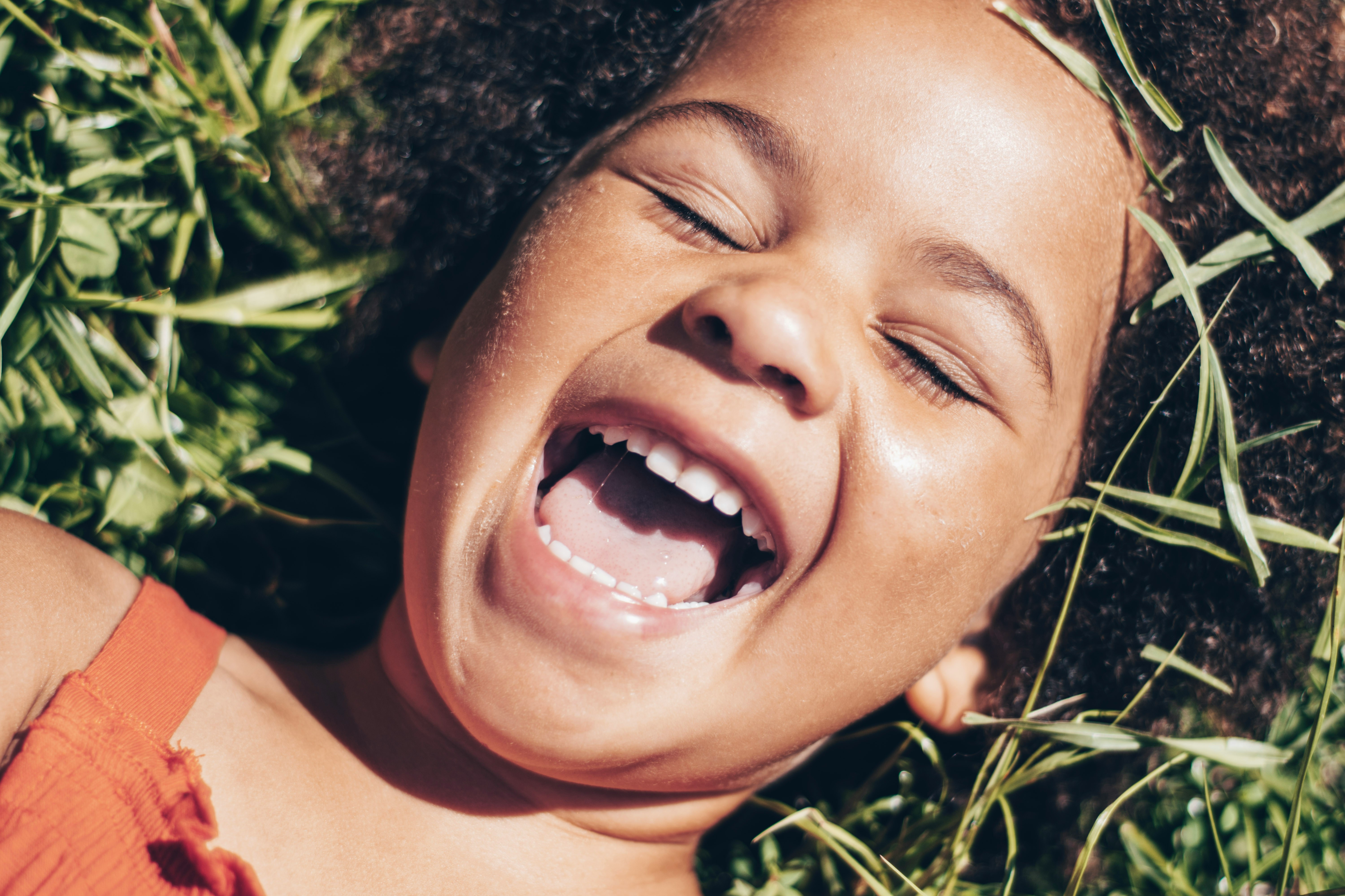 Menina deitada na grama sorrindo, representando a alegria proporcionada pela saúde bucal